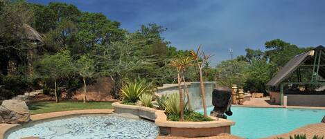 A swimming pool with a hot tub, surrounded by a landscaped garden with rocks and plants.
