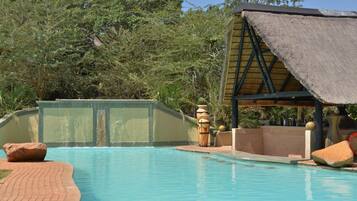 Relax by the serene pool surrounded by lush greenery and a thatched roof seating area.