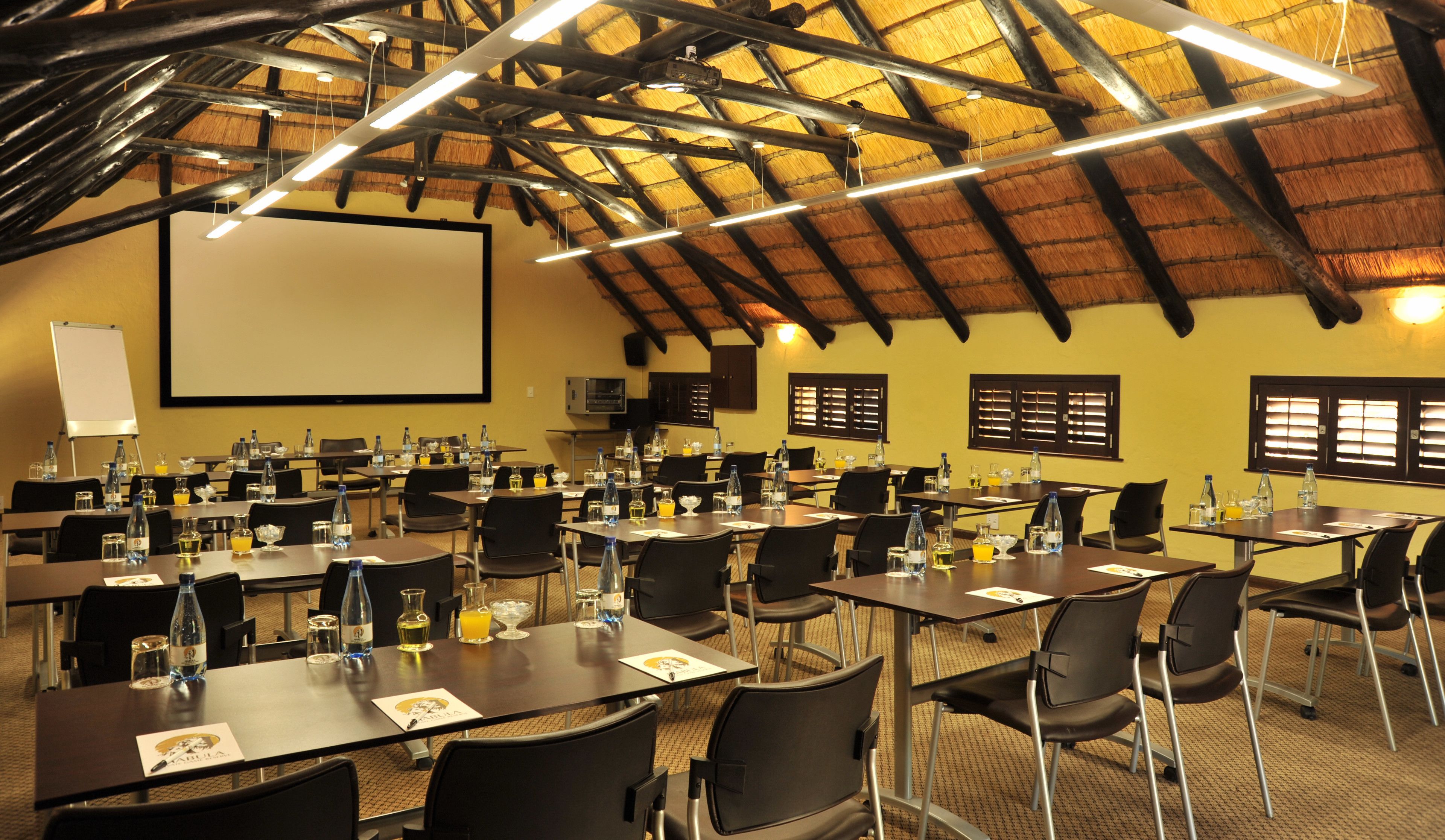 A conference room with multiple tables, chairs, a projector screen, and a large screen.