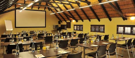 A conference room with multiple tables, chairs, a projector screen, and a large screen.