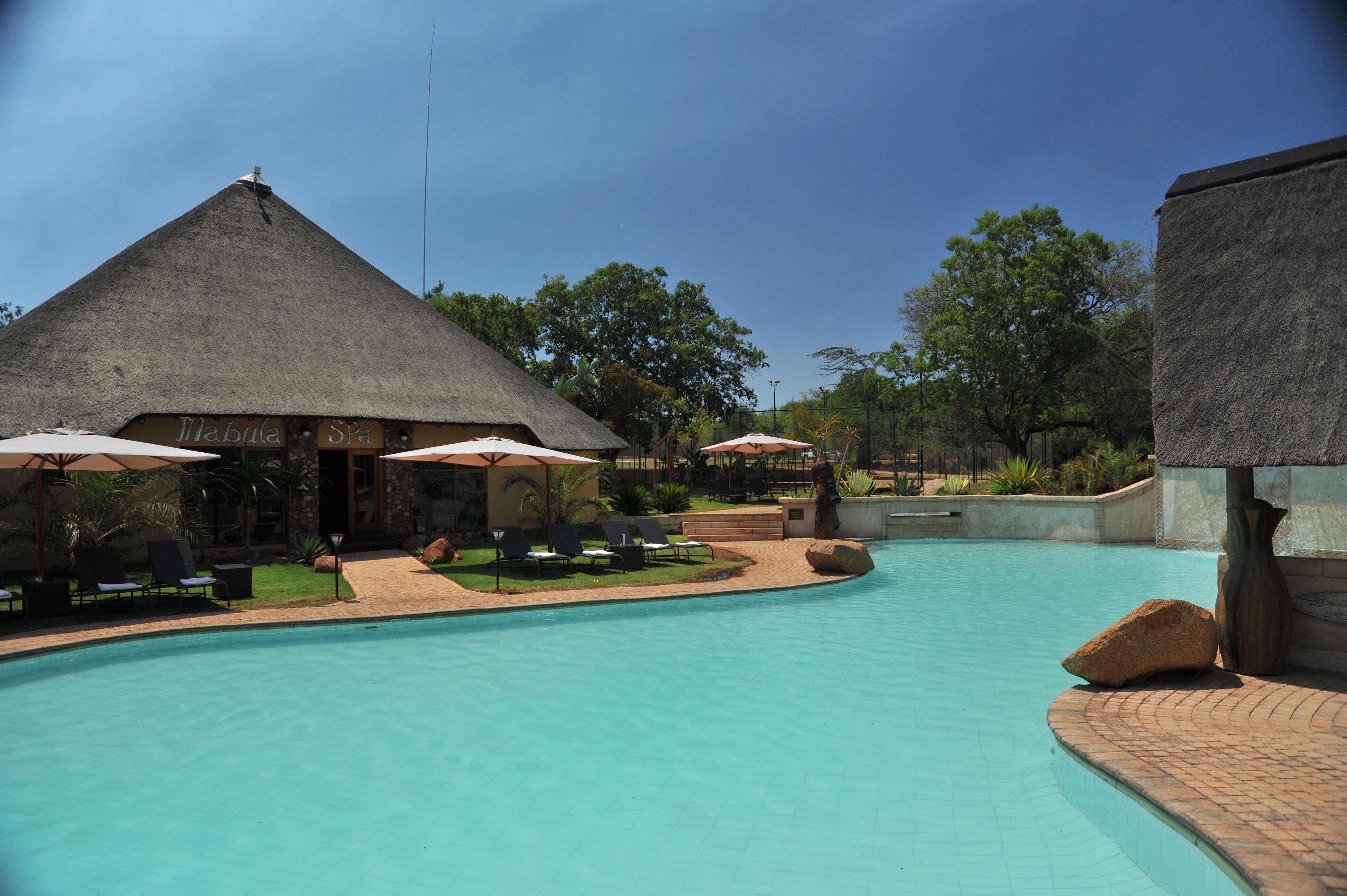 A swimming pool with lounge chairs and umbrellas, a thatched-roof building labeled 'Mabula Spa', and surrounding greenery.