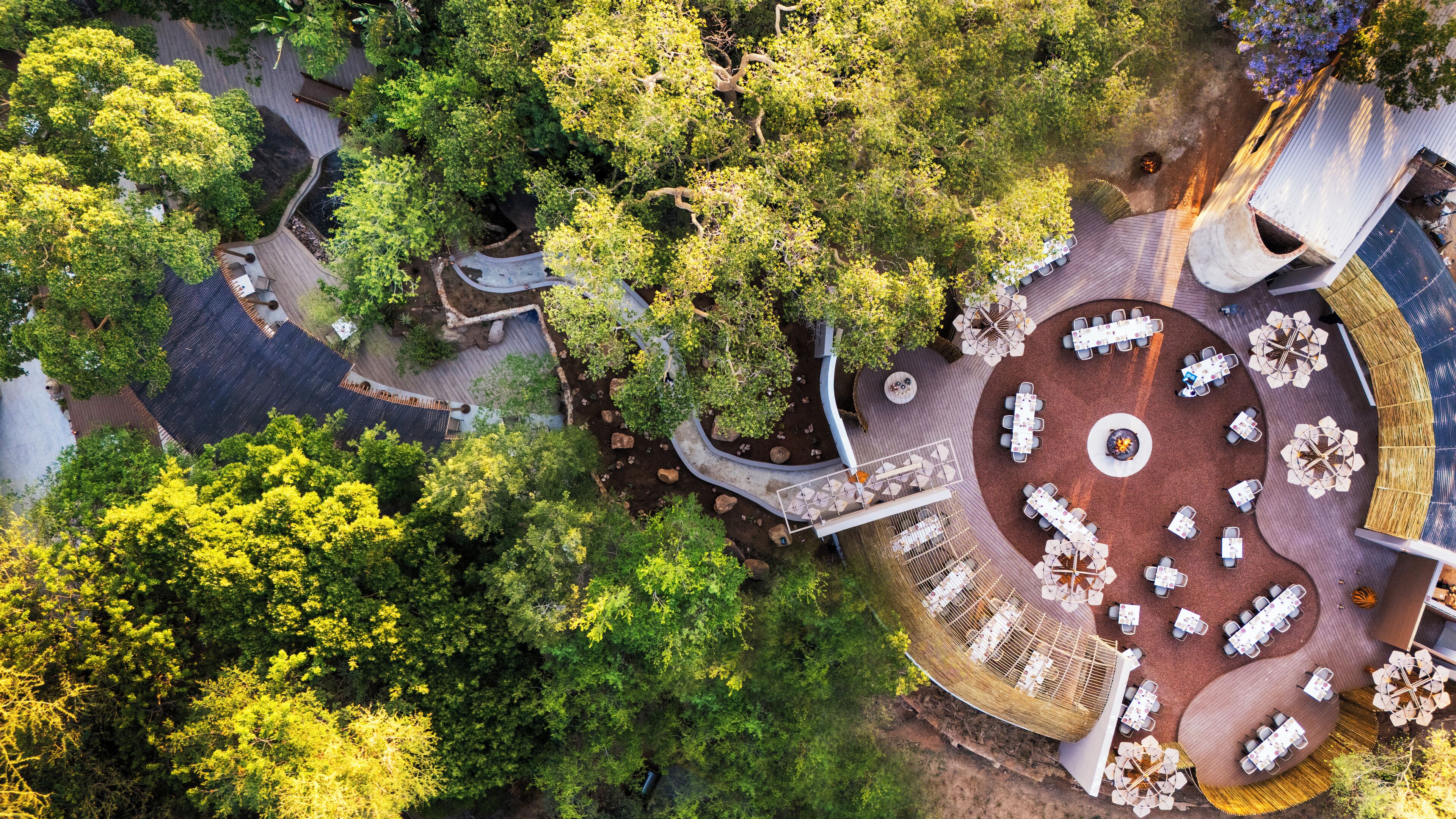 An aerial view of a resort with multiple outdoor dining areas surrounded by lush greenery and trees.