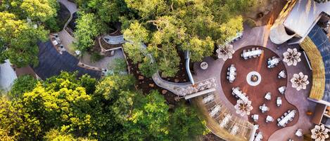 An aerial view of a resort with multiple outdoor dining areas surrounded by lush greenery and trees.