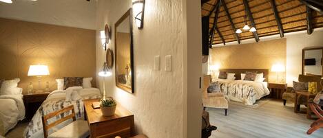 A hotel room with a bed, a desk with a chair, a table with a bowl of fruit, and a dining table with chairs.