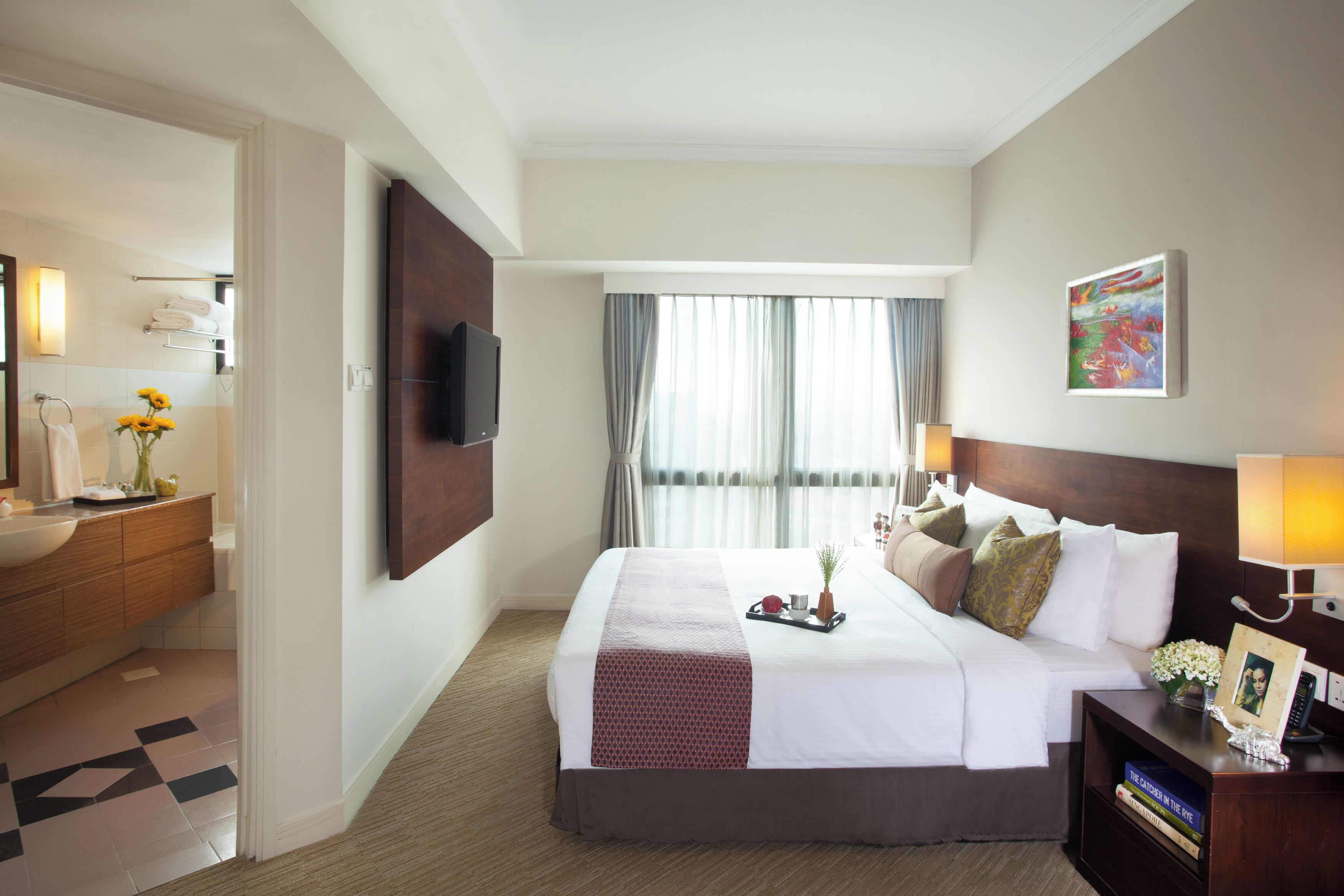 A hotel room with a bed, bedside table, TV, and a bathroom with a sink and towel rack.