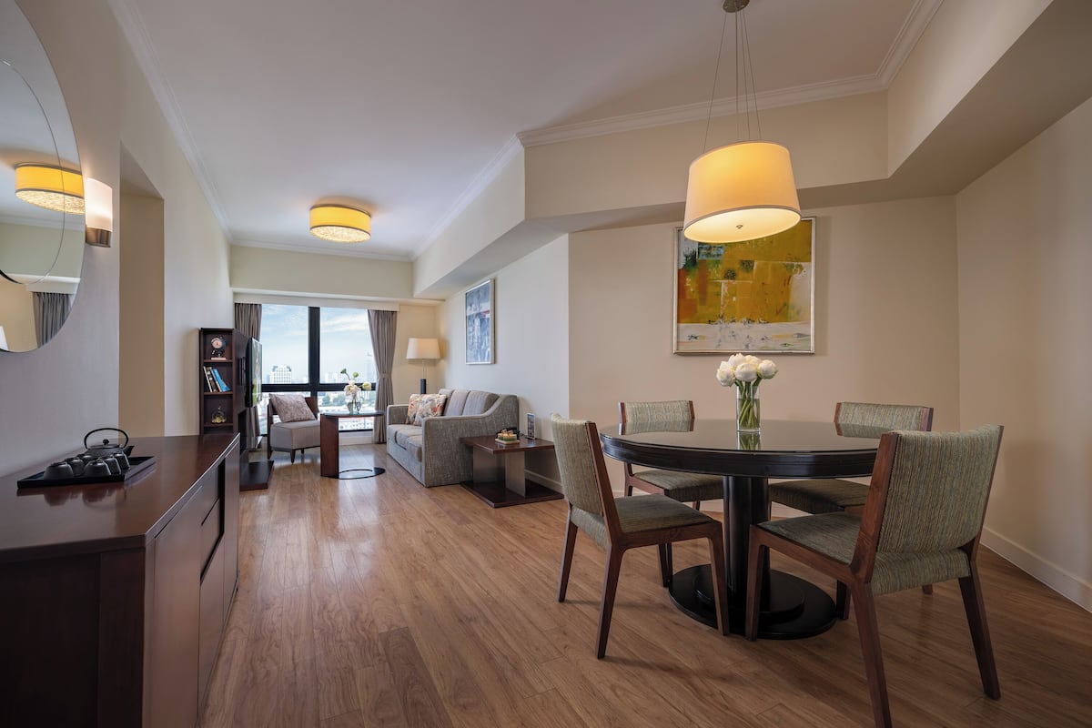 A modern hotel room with a dining area, a sofa, and a TV.