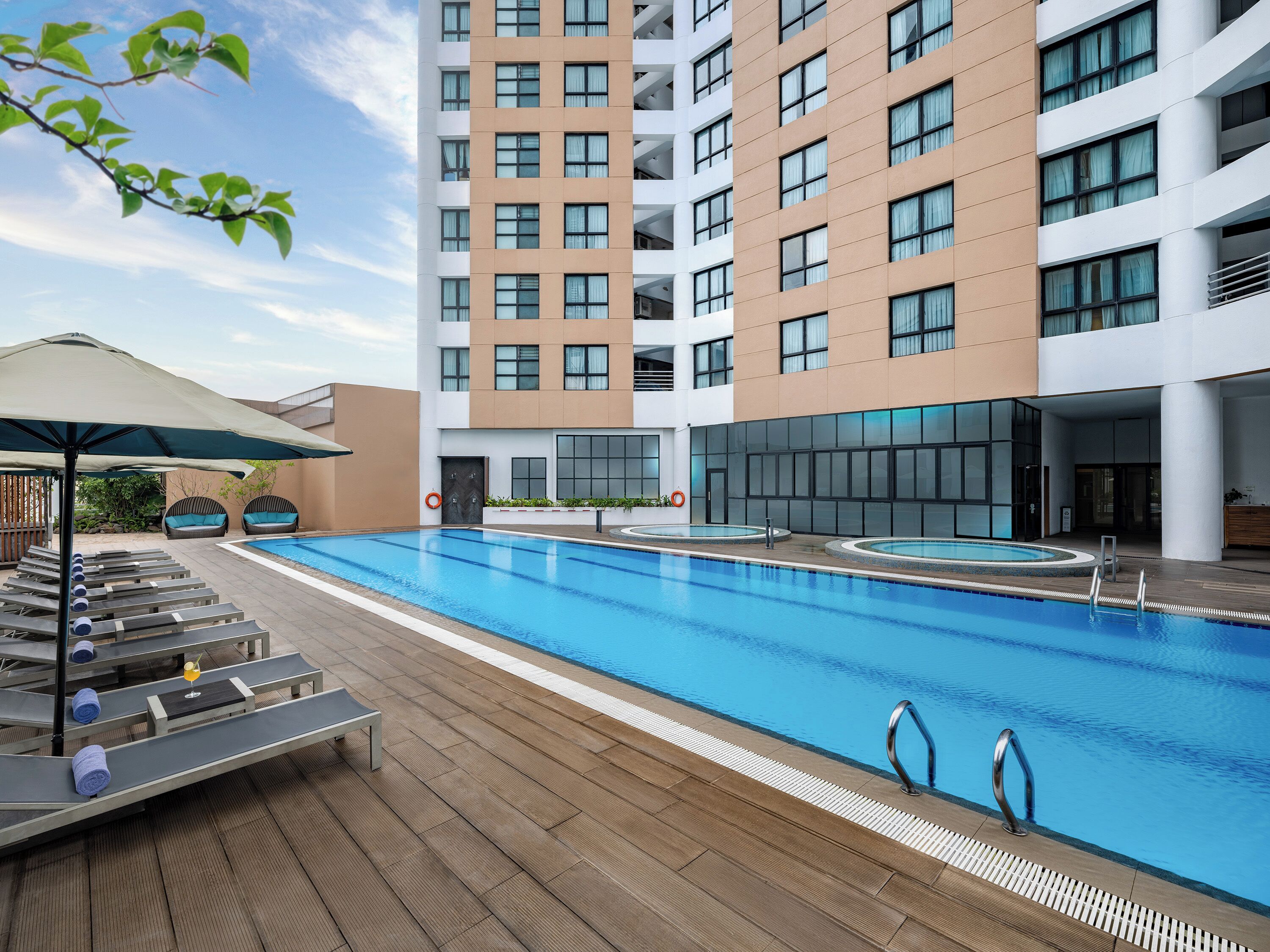 Et moderne hotel med en stor udendørs swimmingpool, liggestole og et overdækket opholdsområde.