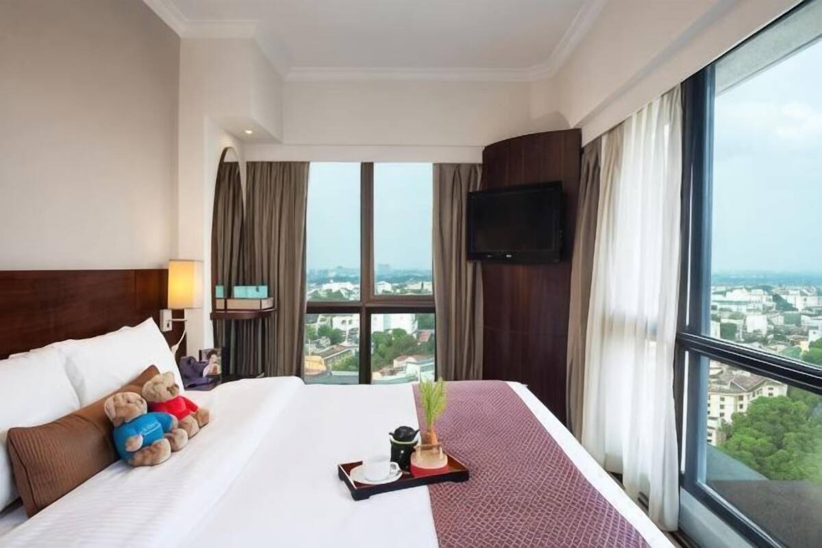 A hotel room with a large bed, a TV mounted on the wall, and a window with a city view.