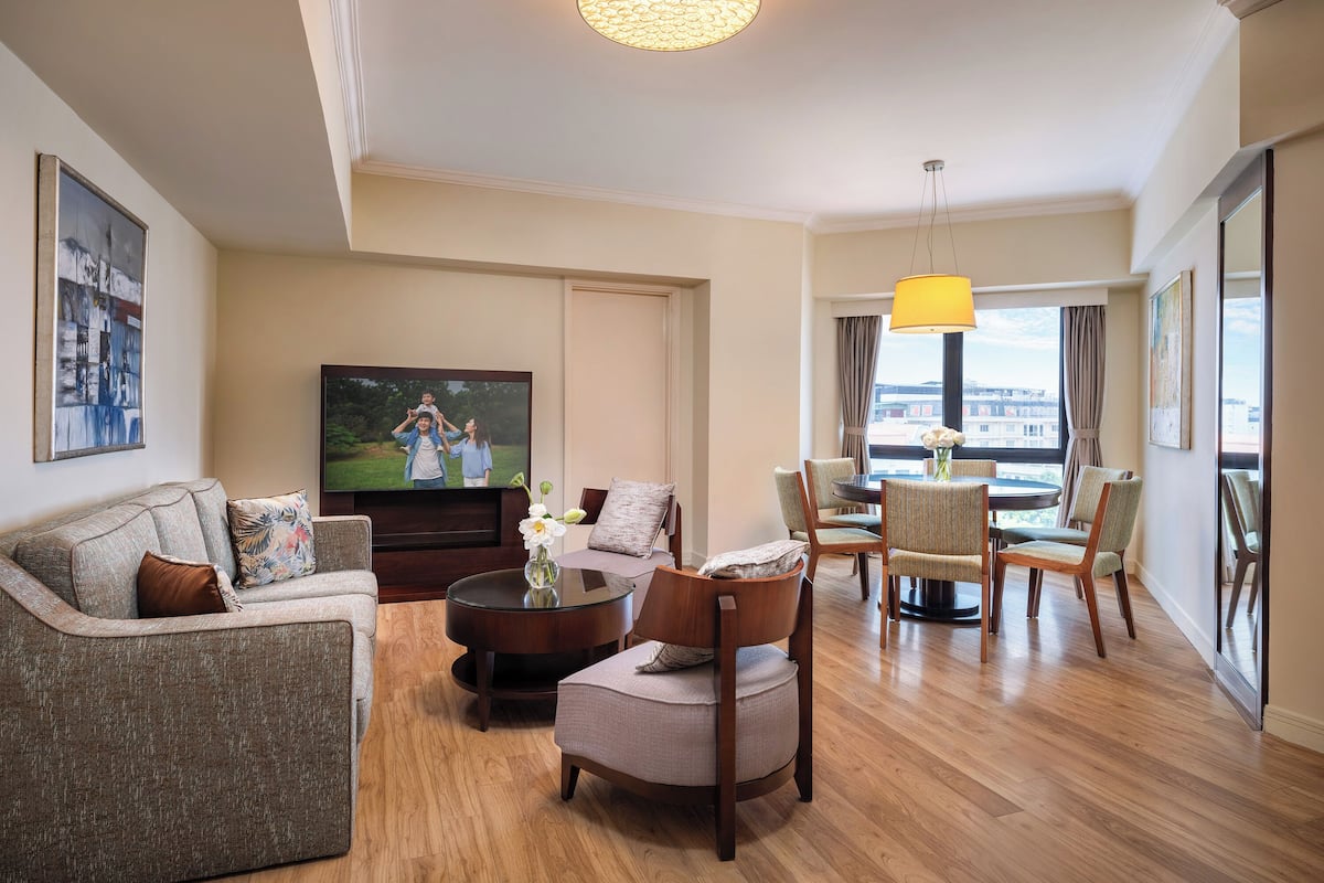 A modern living room with a flat-screen TV, a sofa, a coffee table, and a dining area with chairs and a table.