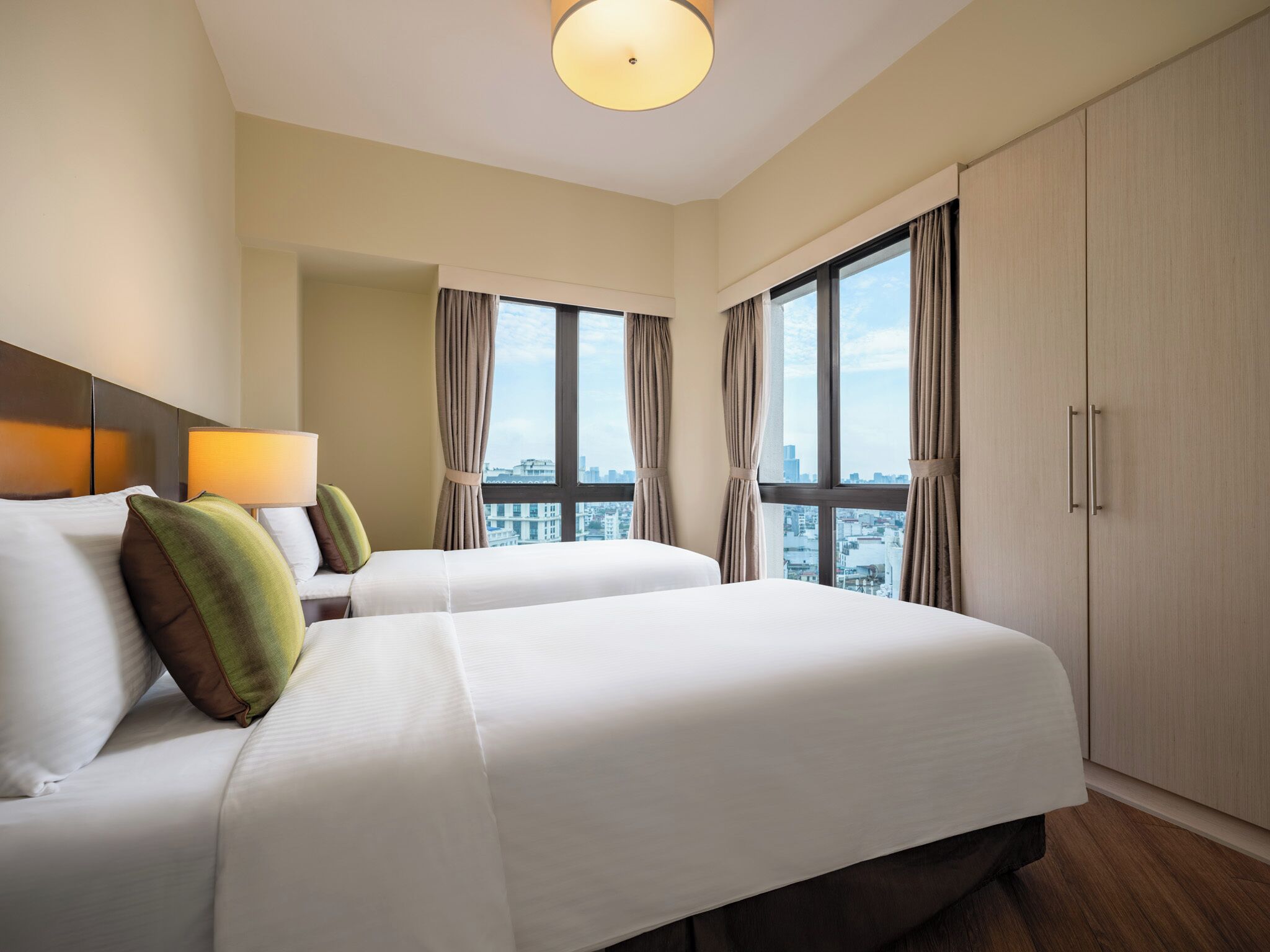 Een hotelkamer met twee bedden, een groot raam, een kledingkast en een plafondlamp.