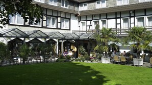 A hotel with a covered outdoor seating area, multiple windows, and a well-maintained garden. - Hotel Bad Griepshop (Hille)