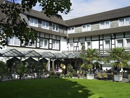 Hotel com área de estar coberta ao ar livre, várias janelas e um jardim bem cuidado.