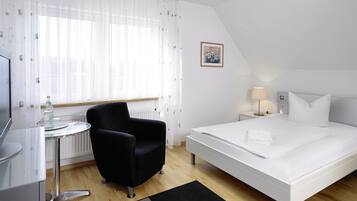 Habitación de hotel con cama, una silla, una mesita, una lámpara y un cuadro en la pared.