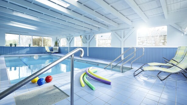 An indoor swimming pool with clear blue water, a diving board, and colorful floating tubes. - Hotel Bad Griepshop (Hille)
