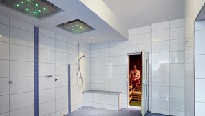 A modern bathroom with white tiled walls, a blue-tiled floor, a bench, and a shower area. - Hotel Bad Griepshop (Hille)