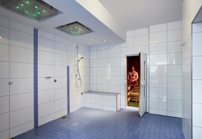 Casa de banho moderna com paredes revestidas de azulejos brancos, chão em azulejos azuis, um banco e zona de duche.