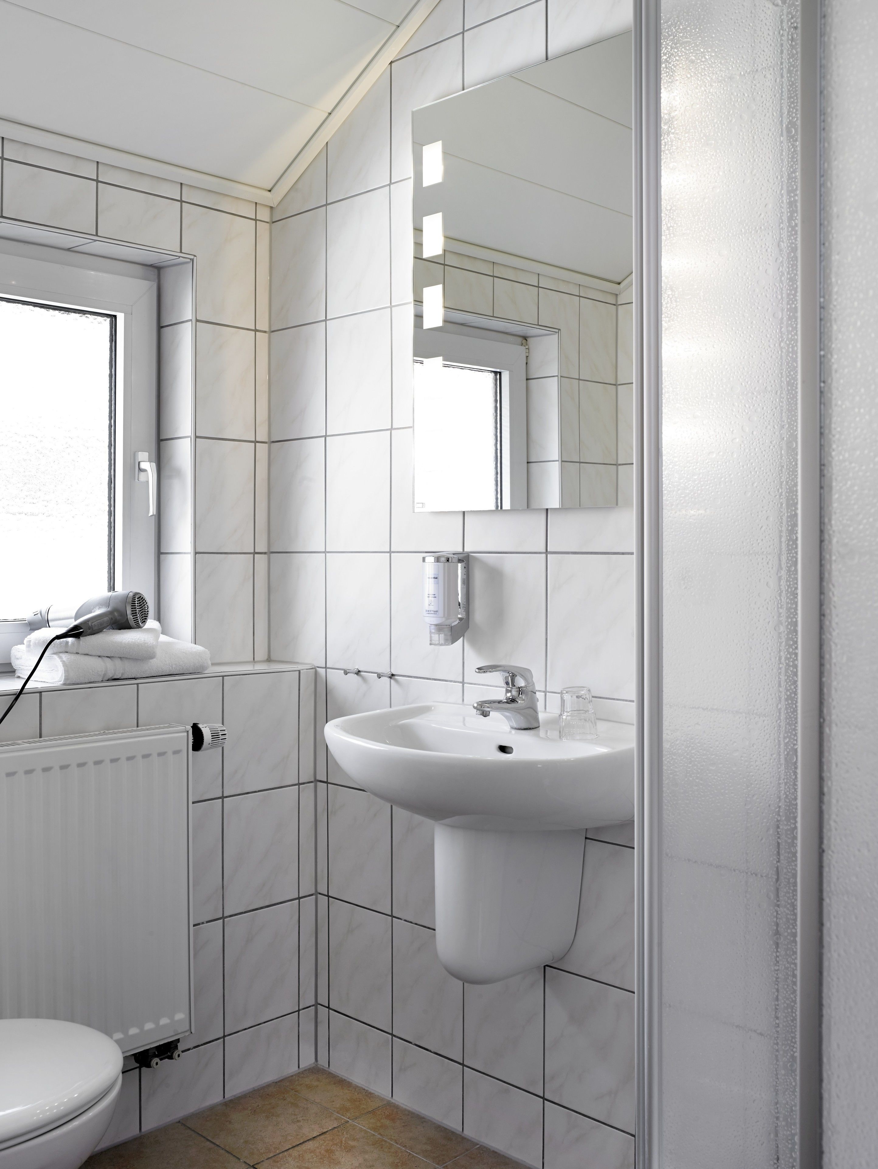 Ein modernes Badezimmer mit weißen Fliesen, einem Waschbecken, einem Spiegel und einer Toilette.