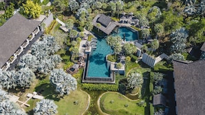 An aerial view of a resort with a central swimming pool, surrounded by palm trees and manicured gardens. - The Slate (Sa Khu)