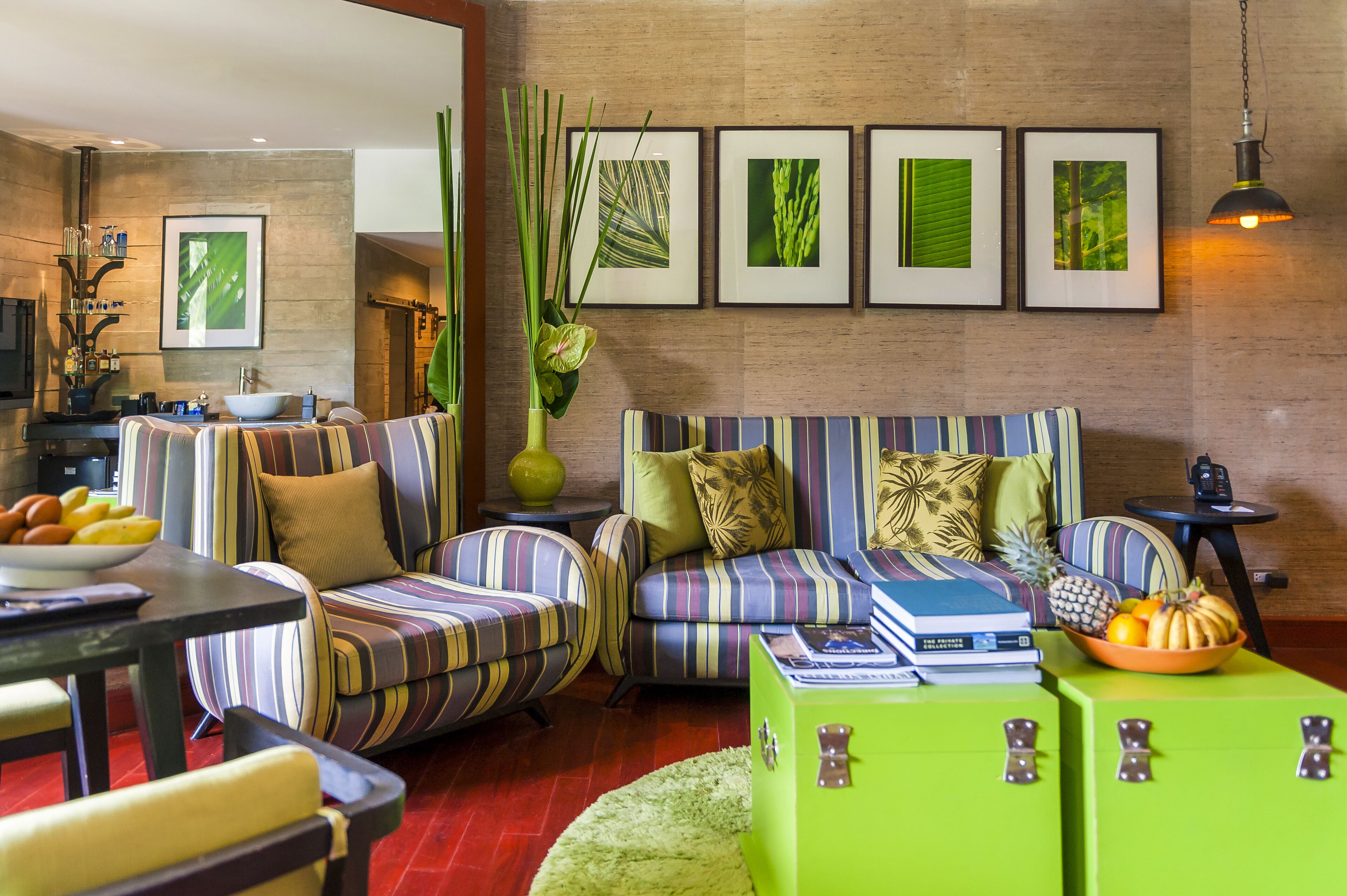 A modern living room with striped sofas, a green coffee table, and a dining area with a bowl of fruit.