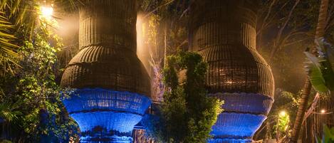 A large, illuminated structure with multiple tiers, surrounded by dense foliage and a pathway leading to it.