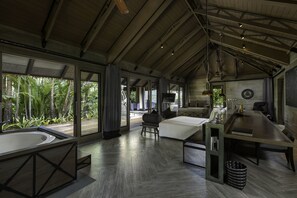 A spacious room with a large bed, a sitting area, and a dining table. There is a large window with curtains, a bathtub, and a view of greenery outside. - The Slate (Sa Khu)