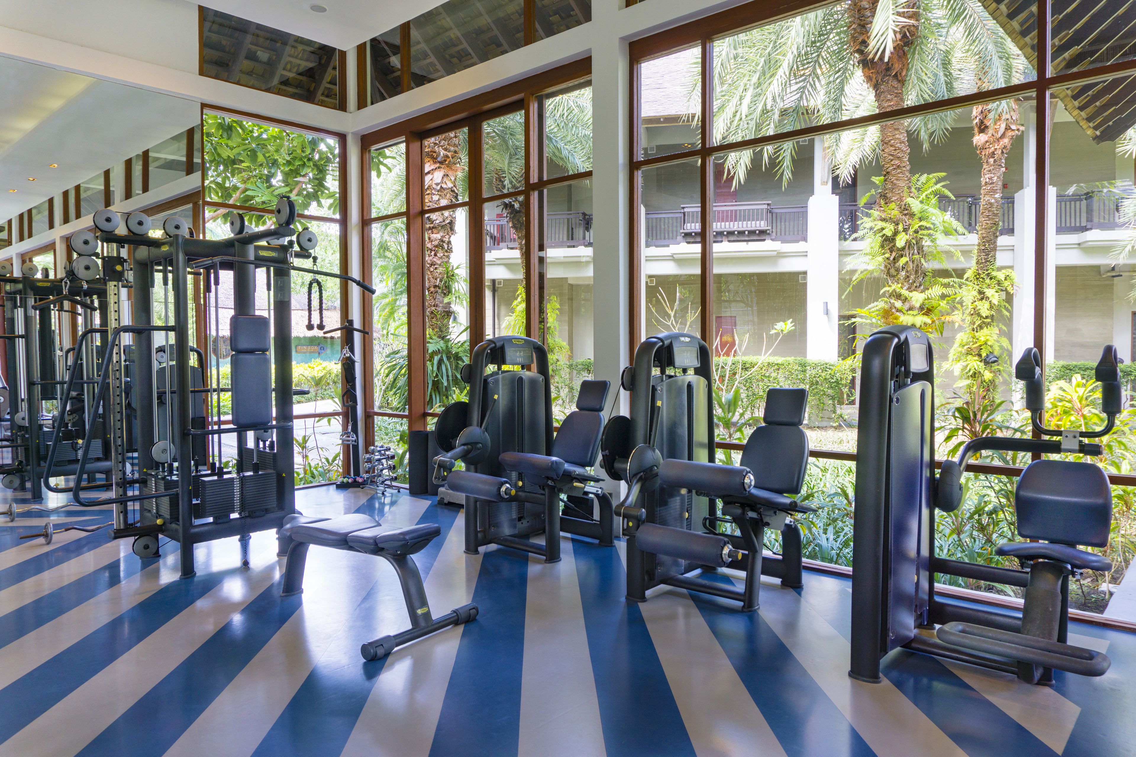 A gym with exercise equipment and large windows overlooking a landscaped area.