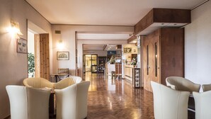 Un vestíbulo de hotel con suelo de madera en dibujo de espiga, una recepción y dos sillones de cuero.