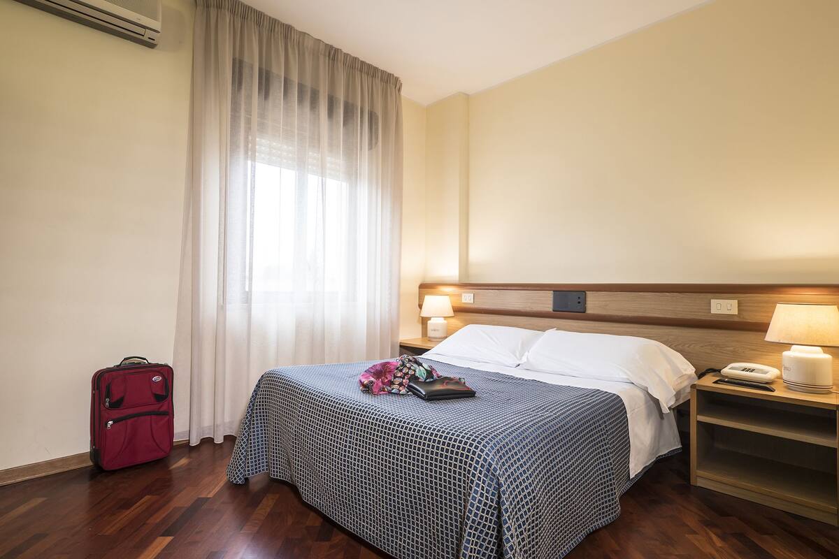 Une chambre d’hôtel avec un lit, une table de chevet, une lampe, un téléphone et une valise.
