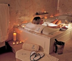 A spa bath with candles, a towel, and a glass of wine.