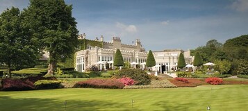 A large, historic building with a formal garden and a well-maintained lawn in front.
