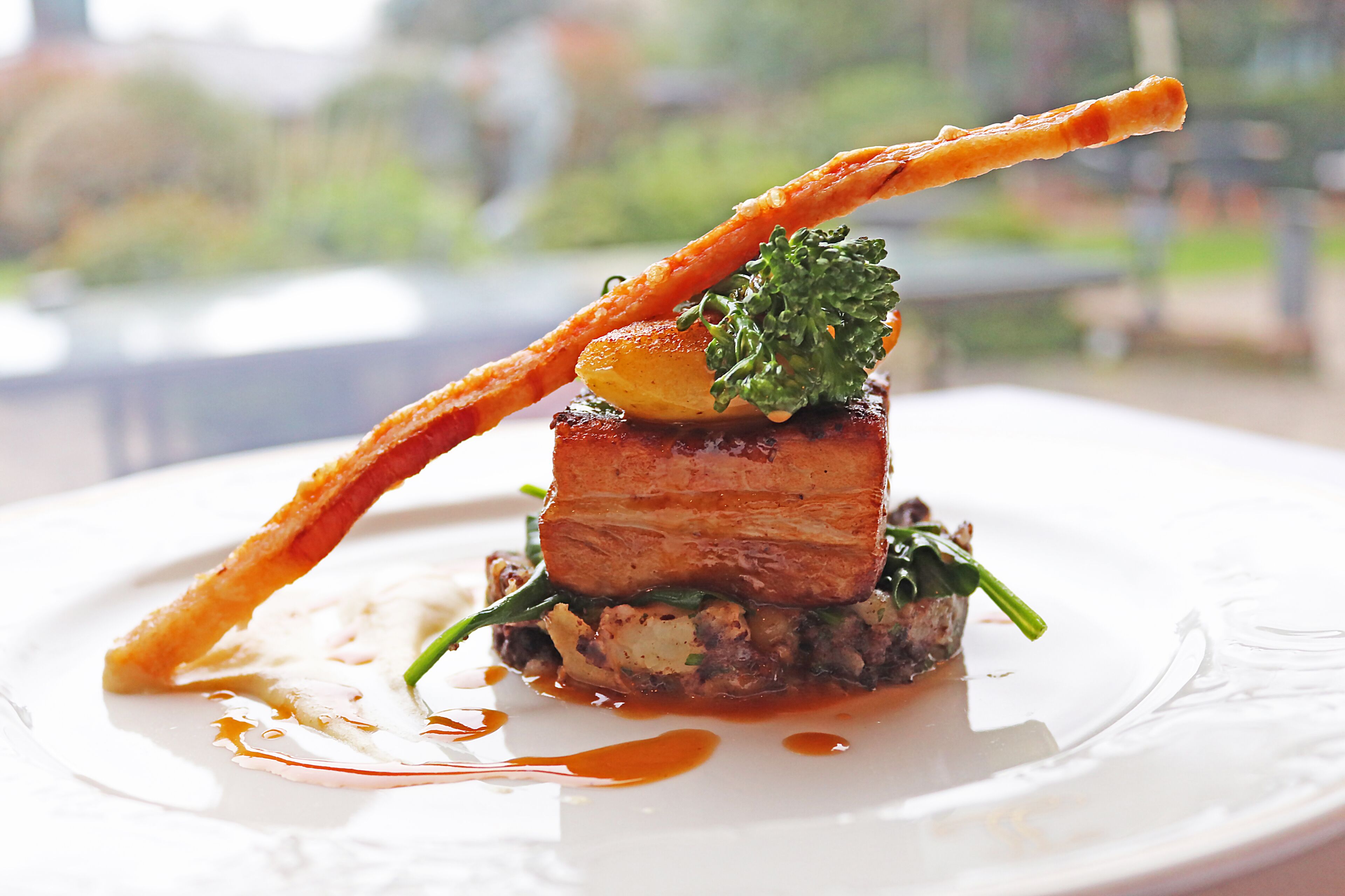 A plated dish with a piece of meat, a vegetable, and a crispy element, possibly a garnish or side.