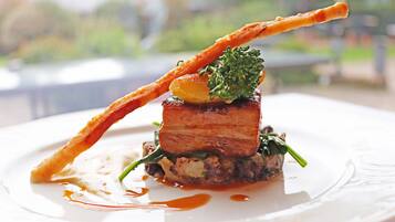 A plated dish with a piece of meat, a vegetable, and a crispy element, possibly a garnish or side.