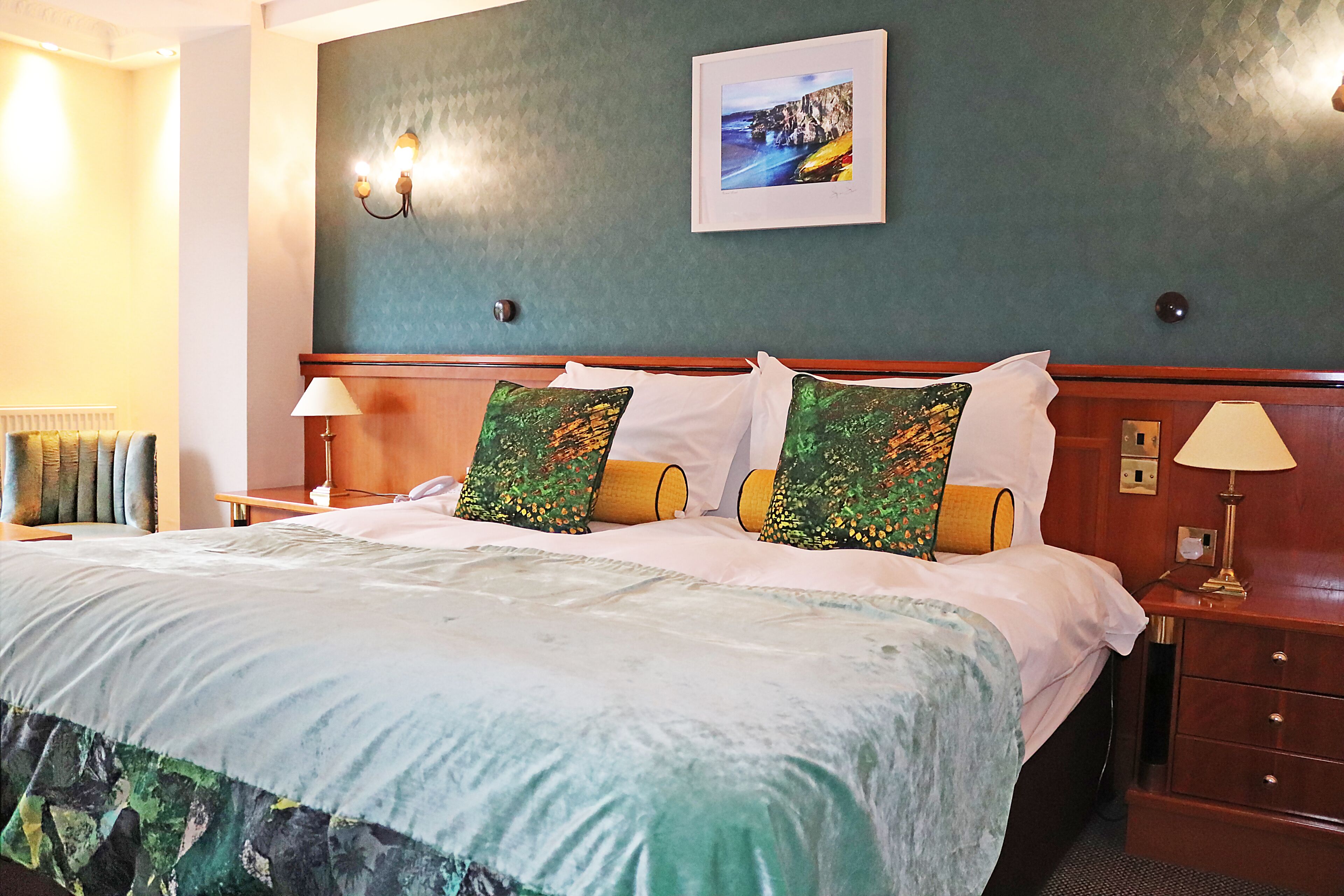 A hotel room with a large bed, two bedside lamps, a framed picture on the wall, and a wooden nightstand.