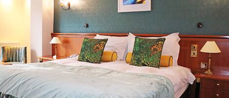 A hotel room with a large bed, two bedside lamps, a framed picture on the wall, and a wooden nightstand.