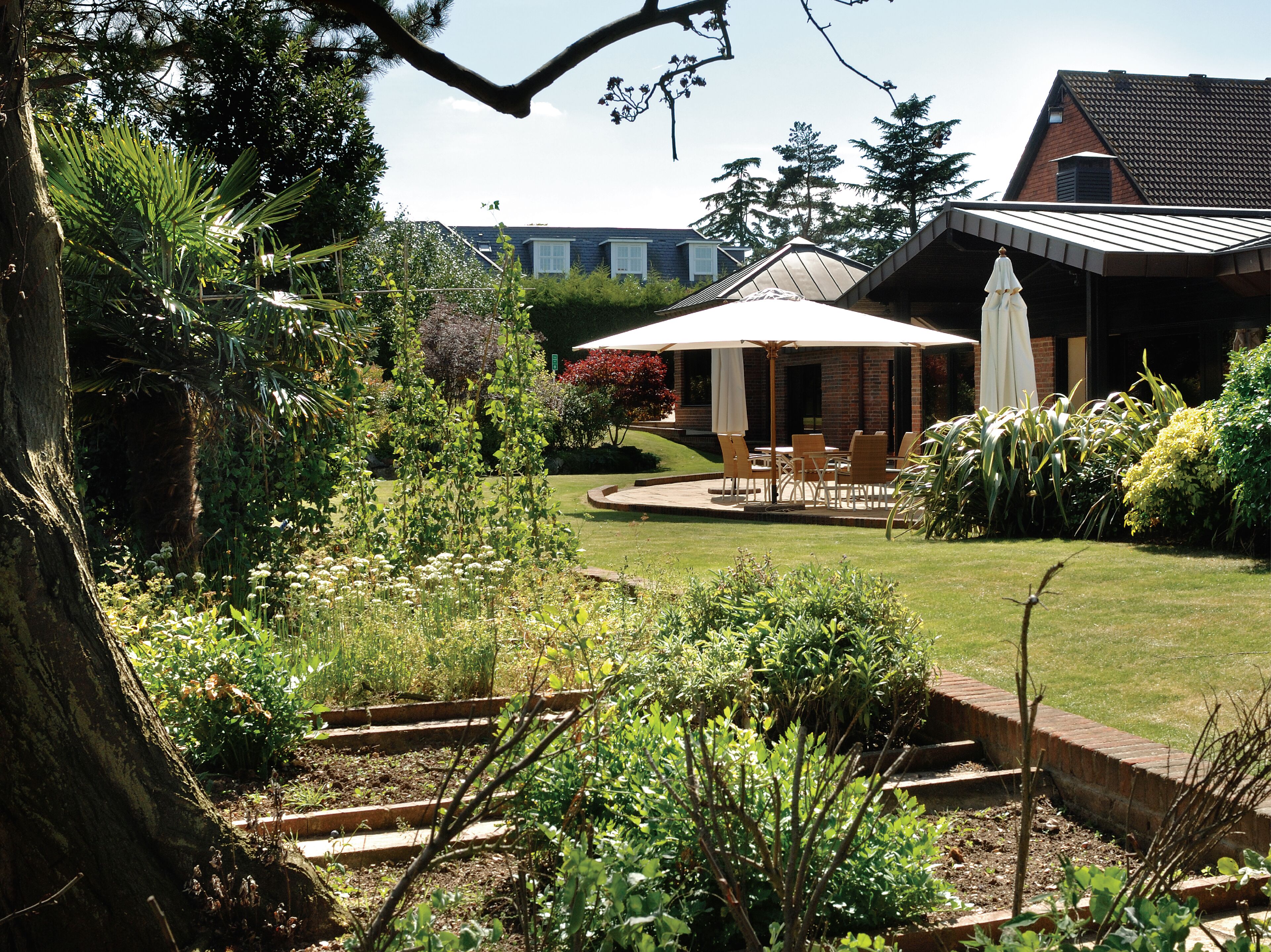 A garden with a patio area, a brick wall, and a building with a sloped roof.