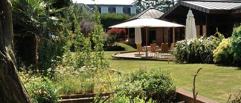 A garden with a patio area, a brick wall, and a building with a sloped roof.