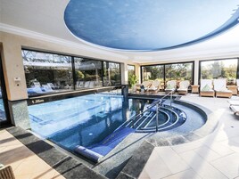 A modern indoor pool with clear blue water, lounge chairs, and a view of the outdoors.