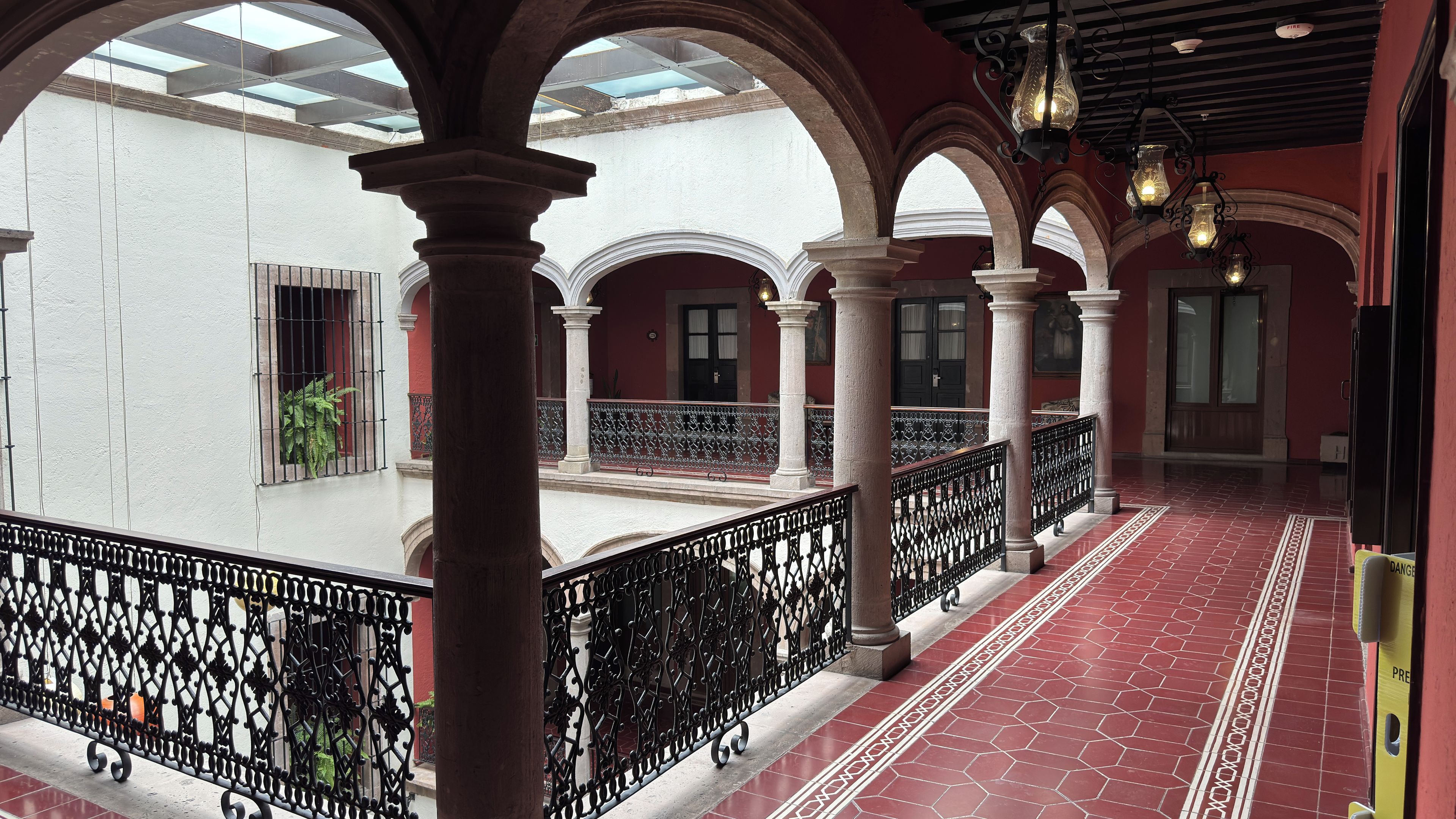 A covered outdoor area with red-tiled flooring, white columns, and black wrought iron railings.