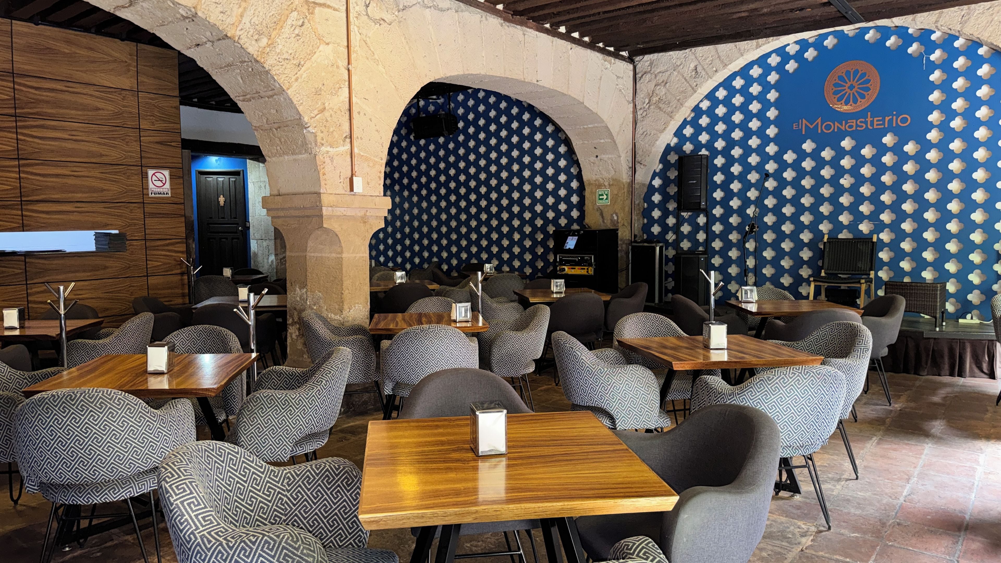 Interior de restaurante con asientos estampados, pared azul con un logo y techo de madera.