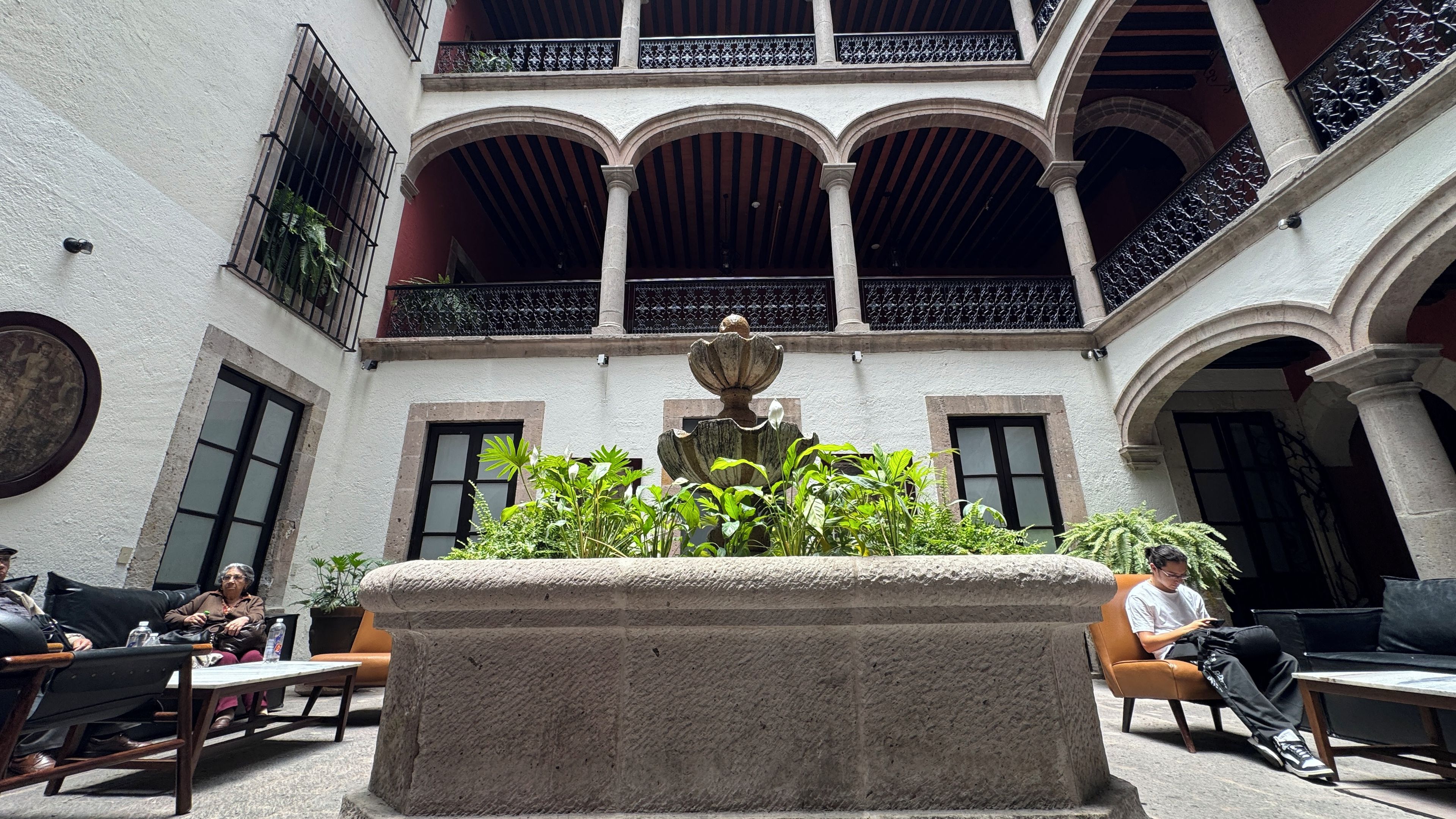 A courtyard with a central fountain, seating areas, and a building with arches and balconies.
