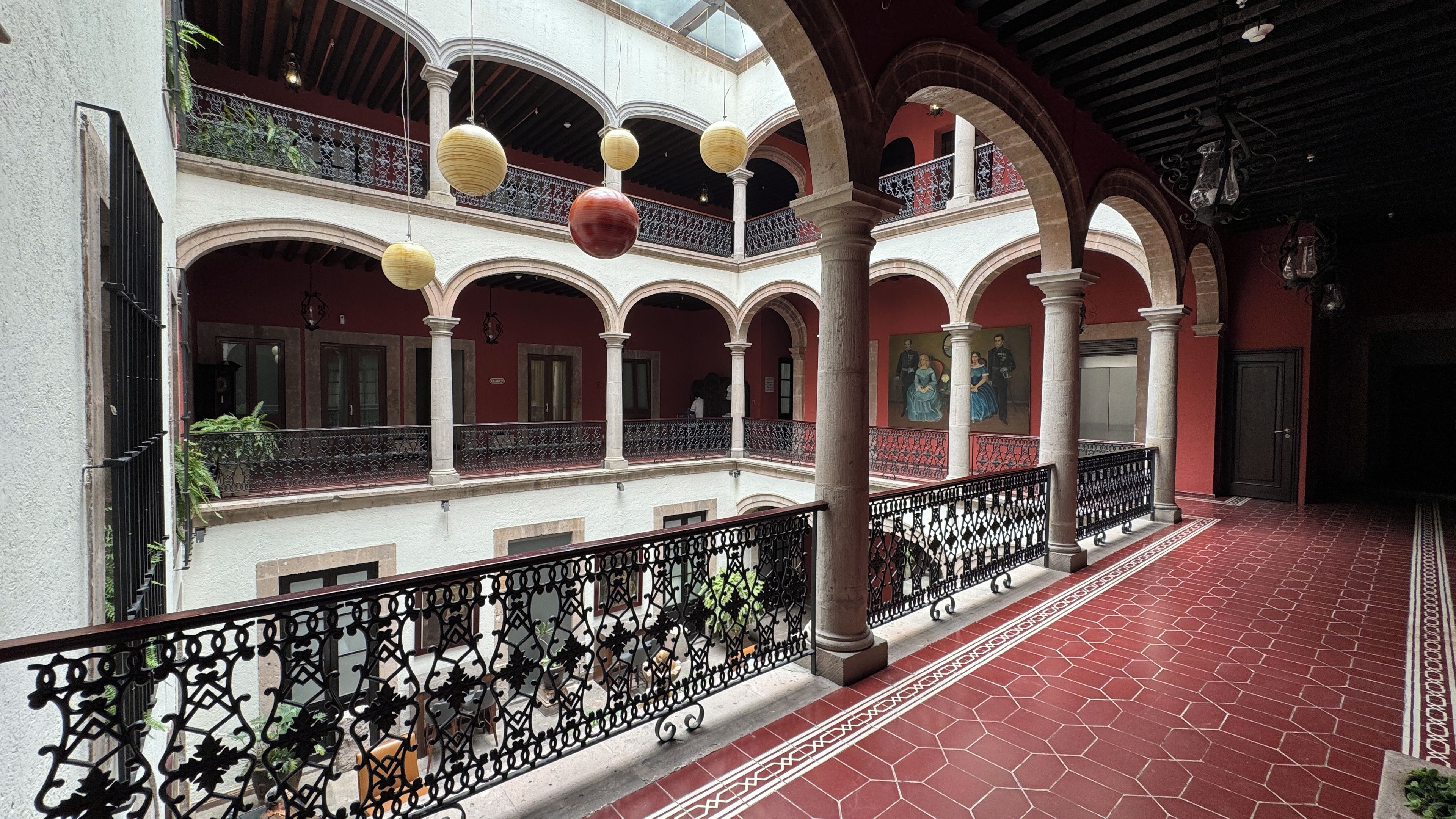 A courtyard with red-tiled flooring, white walls, and black wrought iron railings.