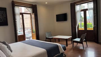 A hotel room with a bed, a desk, a chair, a TV, and a balcony with a view of the city.
