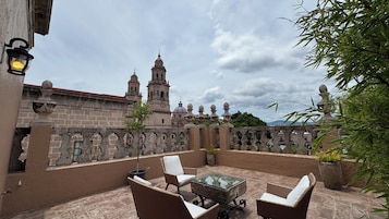 A patio with wicker furniture and a glass table, overlooking a historic building with a bell tower.