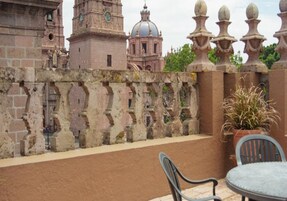 A balcony with a wrought iron railing, a potted plant, and a table with chairs.