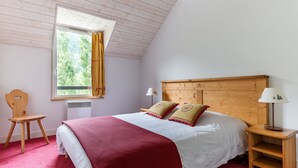 Une chambre à coucher avec une tête de lit en bois, une fenêtre avec des rideaux, une table de chevet avec une lampe et une chaise.