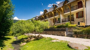 Une rangée de bâtiments en bois dotés de balcons, un mur de pierre et une zone herbeuse traversée par un ruisseau.