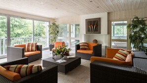 Un vaste espace de vie agrémenté de meubles en osier, de grandes fenêtres et d’un plafond avec des poutres en bois.