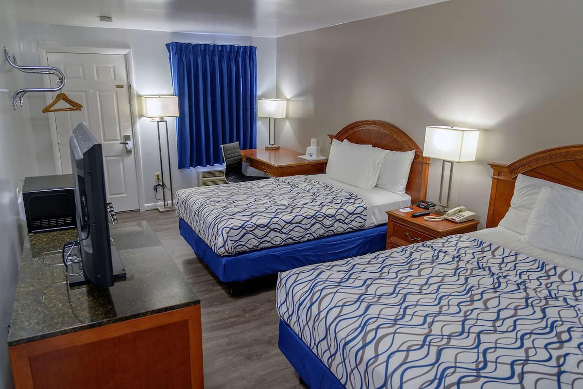 A hotel room with two beds, a desk with a computer, a chair, a lamp, and a telephone.