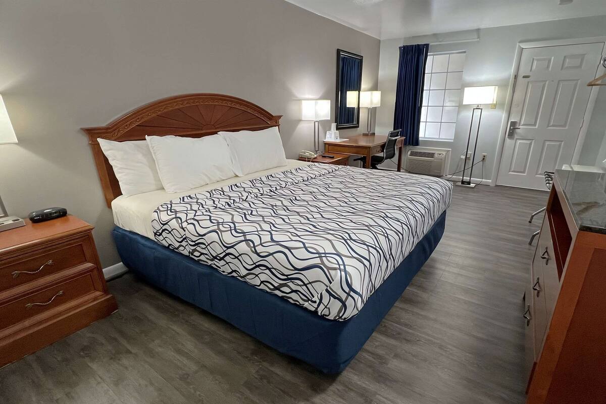 A hotel room with a large bed, wooden headboard, bedside tables, a desk, and a chair.