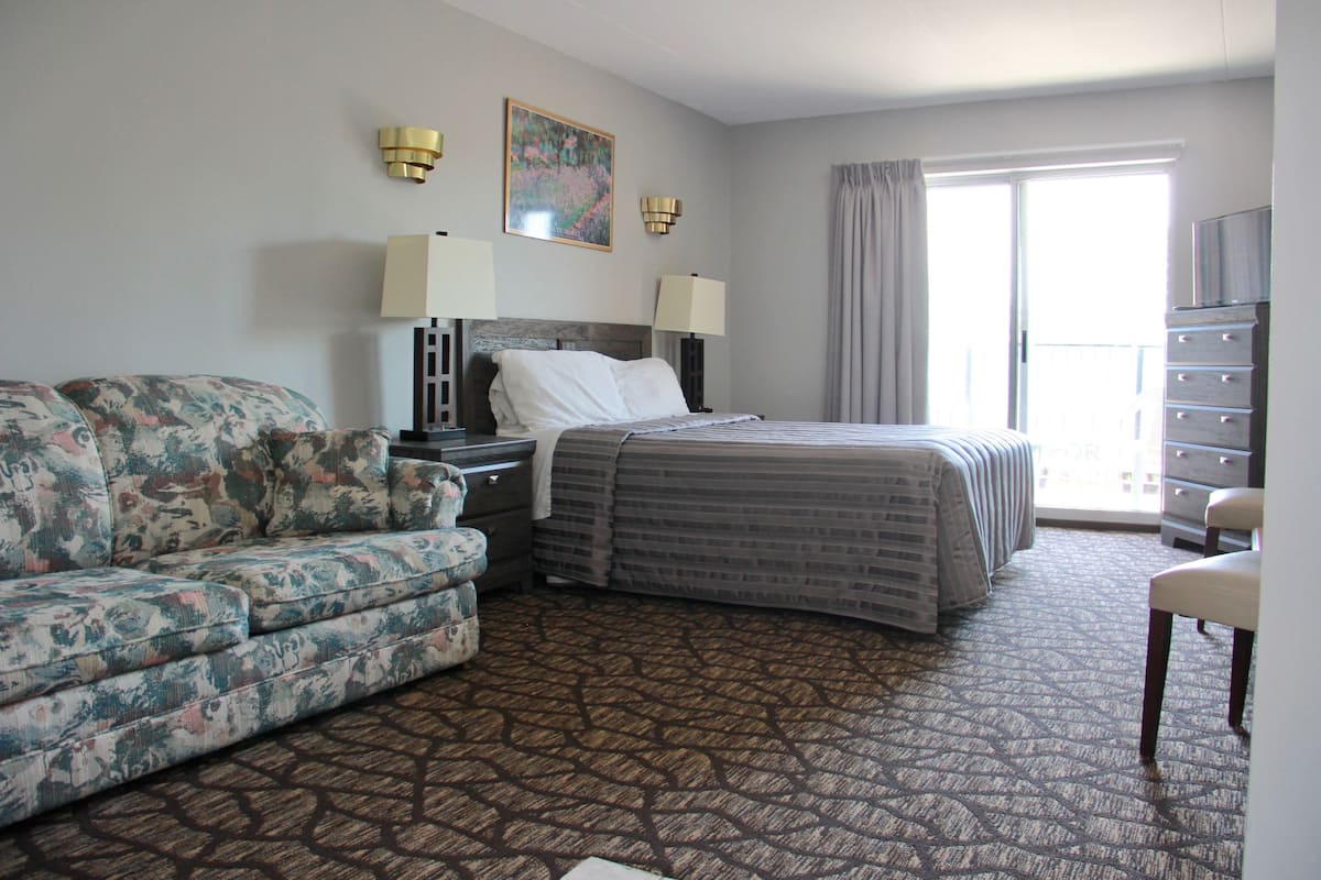 A hotel room with a bed, a sofa, a dresser, and a chair.